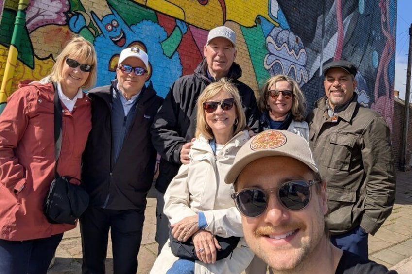 En gruppe mennesker står foran en farverig mural. 4