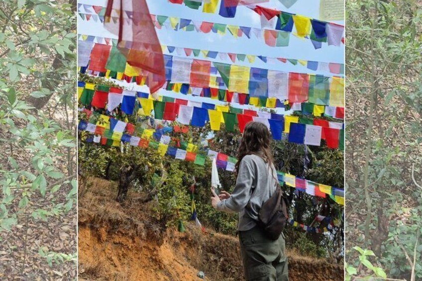 A person taking a photo with colorful prayer flags strung across a hillside. 4