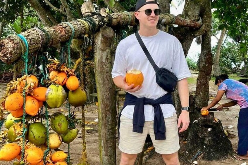 En person holder en kokosnød, stående ved siden af et træ med kokosnødder i grenene. 3