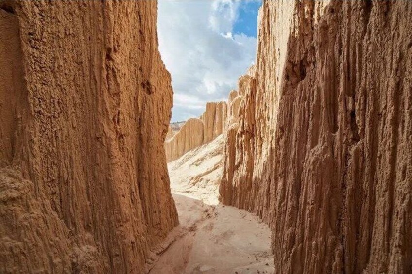 A narrow canyon with steep, eroded rock walls and a clear sky. 5