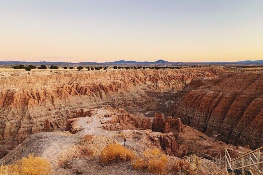 A rugged canyon landscape with layered rock formations and a wooden walkway. 2