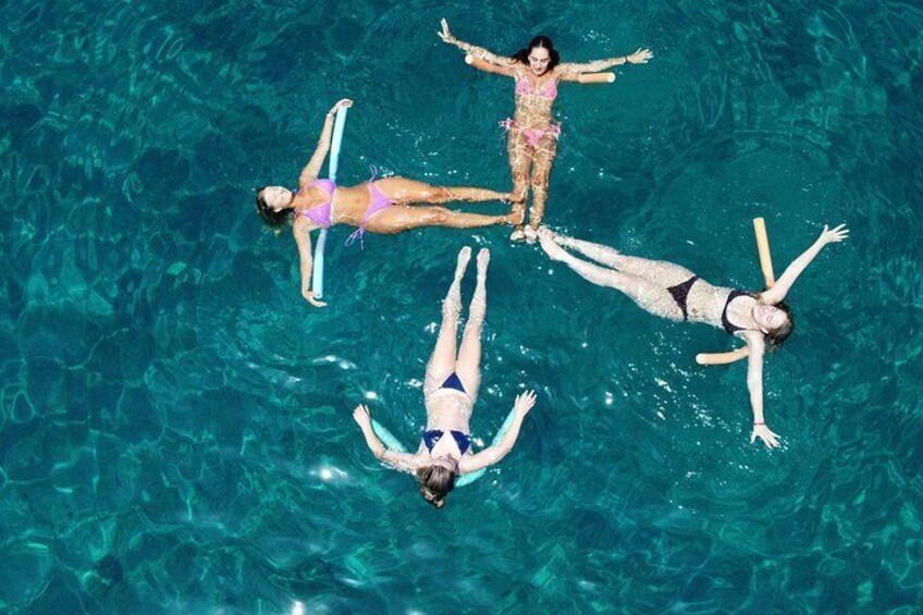 Four people floating in a clear blue pool. 4