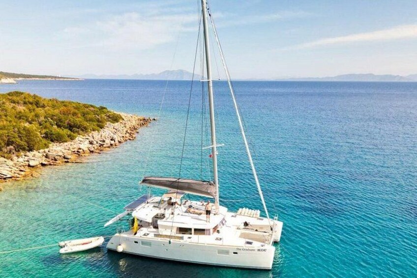 A sailboat anchored near a rocky shoreline with clear turquoise water. 2