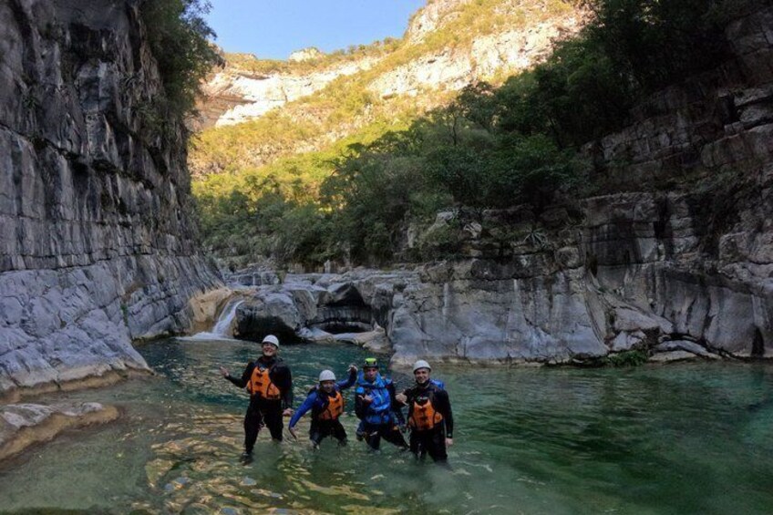 A group of people in a canyon with a river, rocky cliffs, and greenery. 2