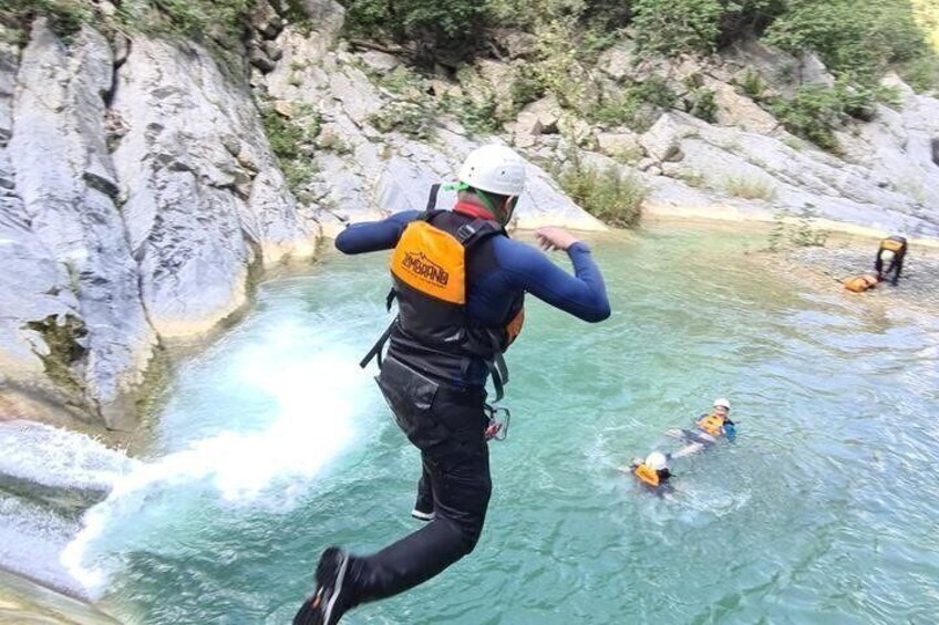 A person jumping into a river from a cliff, wearing a helmet and life jacket. 5