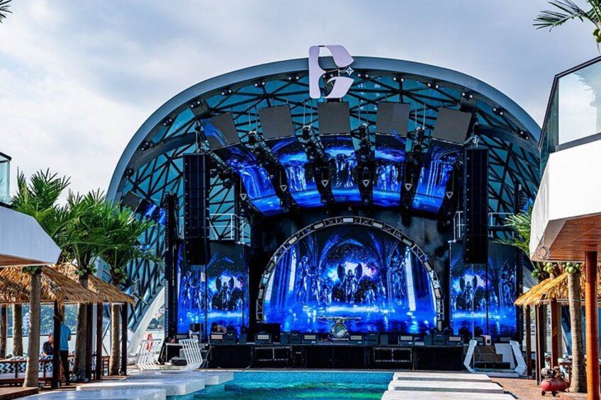 Een groot open podium met een cirkelvormig ontwerp, omgeven door palmbomen en een zwembad. 4