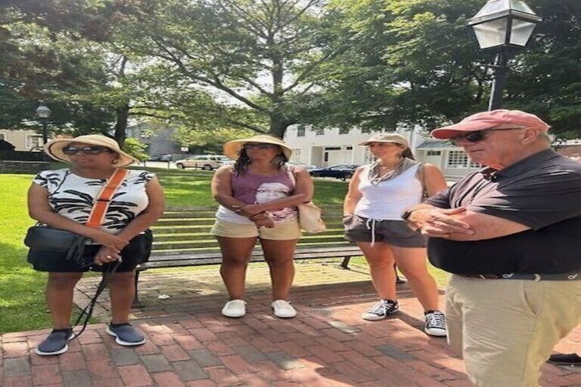 A group of people standing on a brick pathway in a park with trees and a lamp post in the background. 5