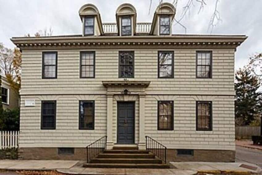 A two-story building with a central entrance, a small porch, and a symmetrical facade. 2