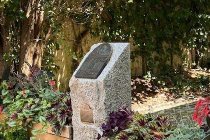 A stone monument with engraved text, surrounded by lush greenery and a stone wall. 3