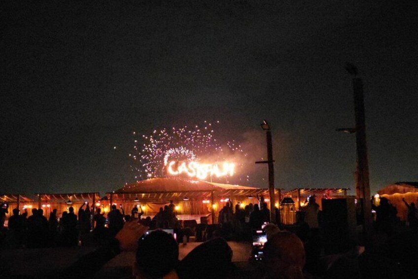 A nighttime outdoor event with a crowd, fireworks, and a tented area. 2