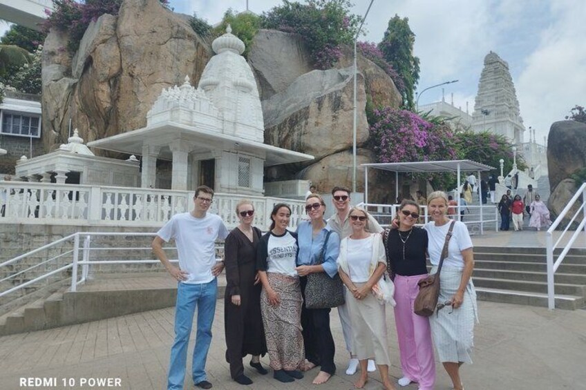 En gruppe mennesker poserer foran et tempel med store klippeformationer og en trappe i baggrunden. 4