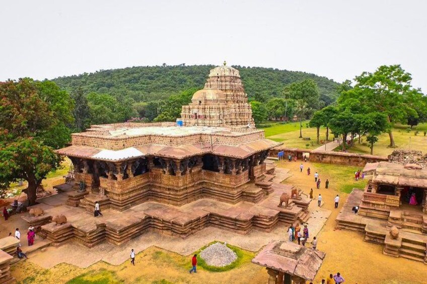 A large, ancient temple complex with multiple structures, surrounded by lush greenery and a hilly backdrop. 1