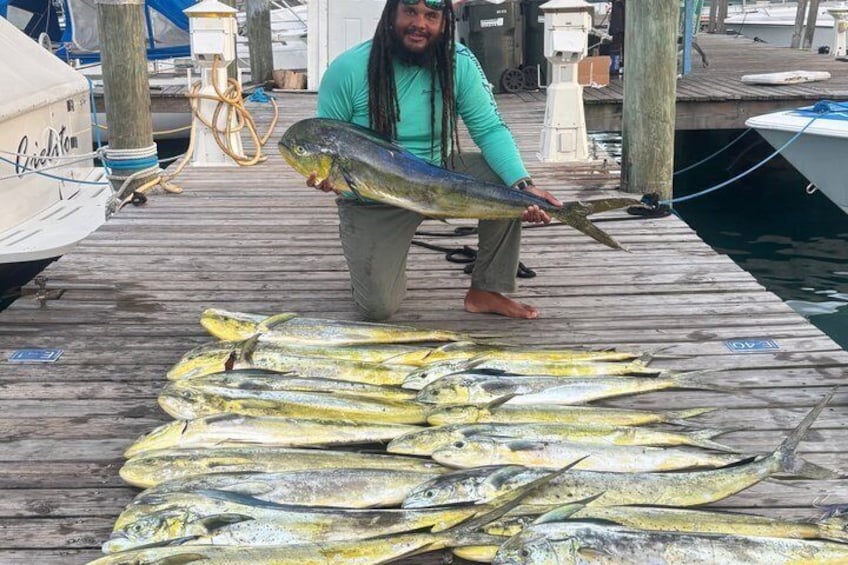 En person holder en stor fisk på en bro, mens flere mindre fisk ligger udstillet foran. 1