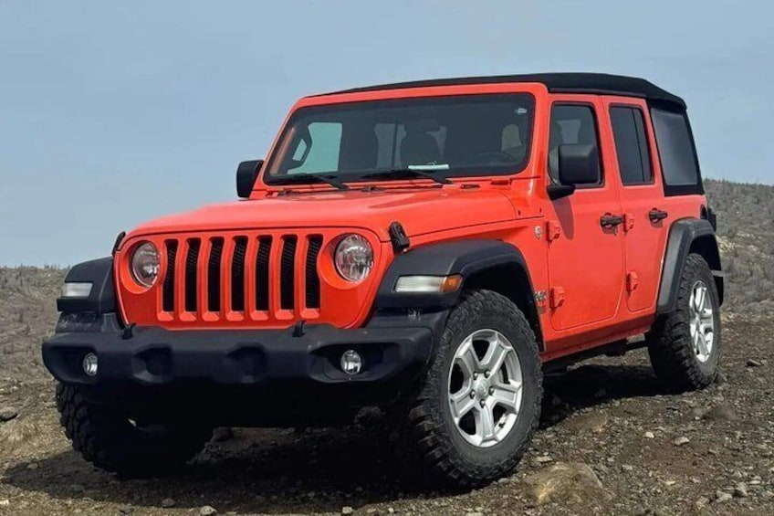 Un Jeep Wrangler rosso con pneumatici da fuoristrada e tetto nero, parcheggiato su un terreno roccioso. 1
