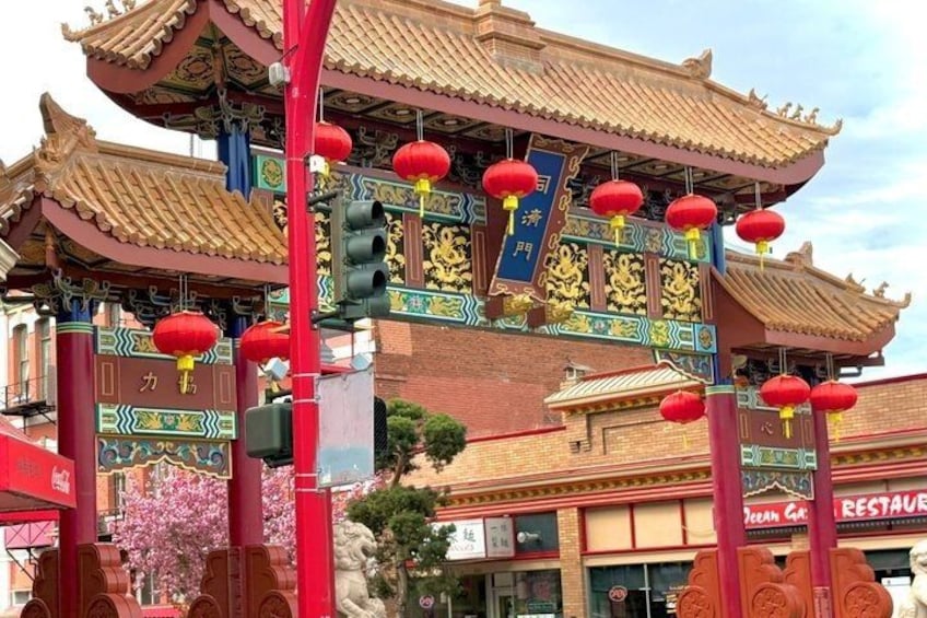 Ein traditionelles chinesisches Tor mit roten Laternen, aufwendigen goldfarbenen Verzierungen und einem Schild mit chinesischen Schriftzeichen. 3