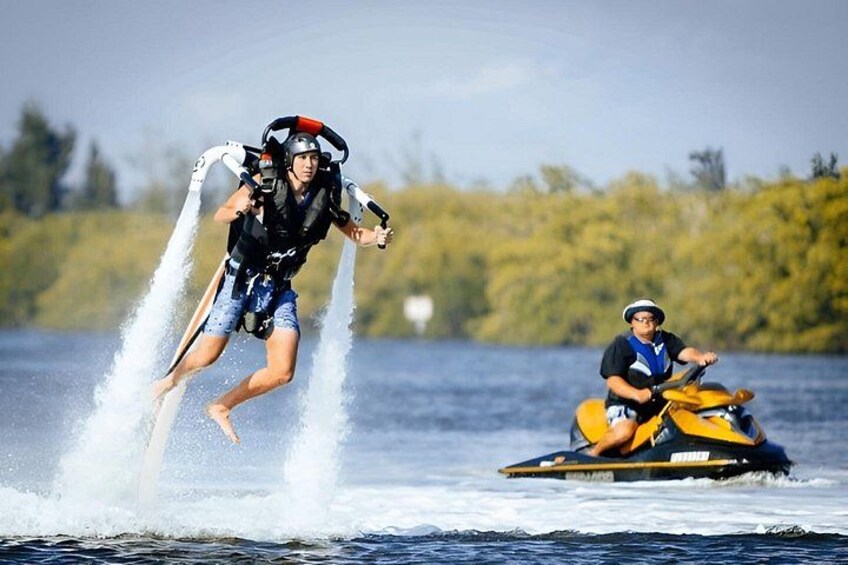 Una persona esquiando acuáticamente tras un jet ski, otra persona en un jet ski, y un cuerpo de agua con árboles al fondo. 4