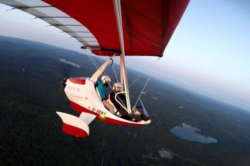 En hangglider med rød vinge svæver over et skovlandskab. 4