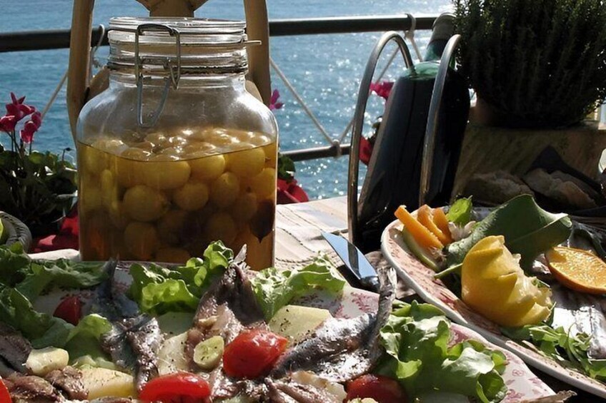 Ett picknickbord med mat, en burk oliver och utsikt över havet. 1