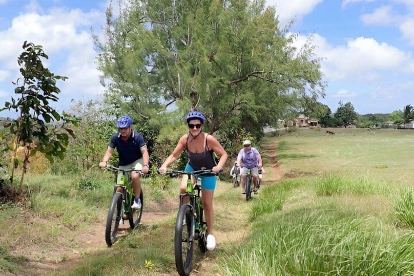 Two cyclists on a dirt path with grass and trees in the background. 1
