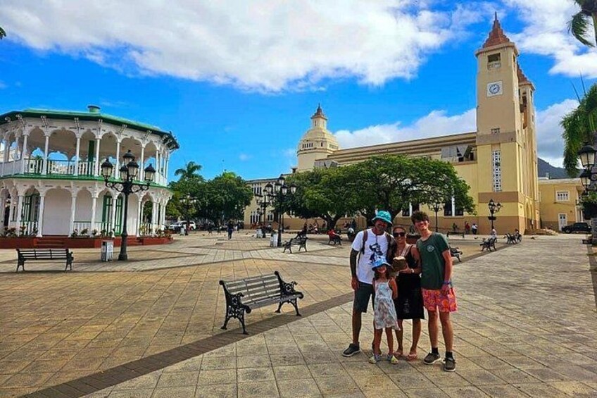 A plaza with a clock tower, a round building, and people standing. 3