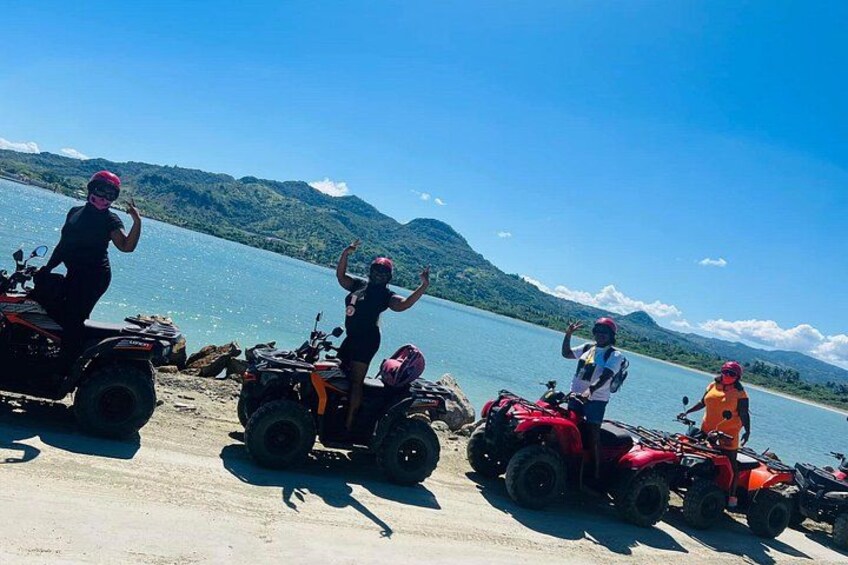 Three people on ATVs by a lake with mountains in the background. 5