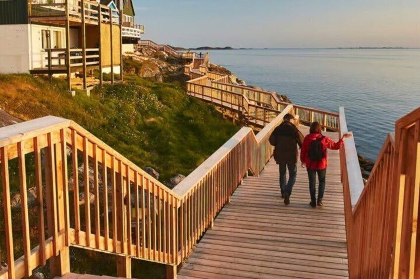 A wooden boardwalk leading to a coastal area with buildings in the background. 2