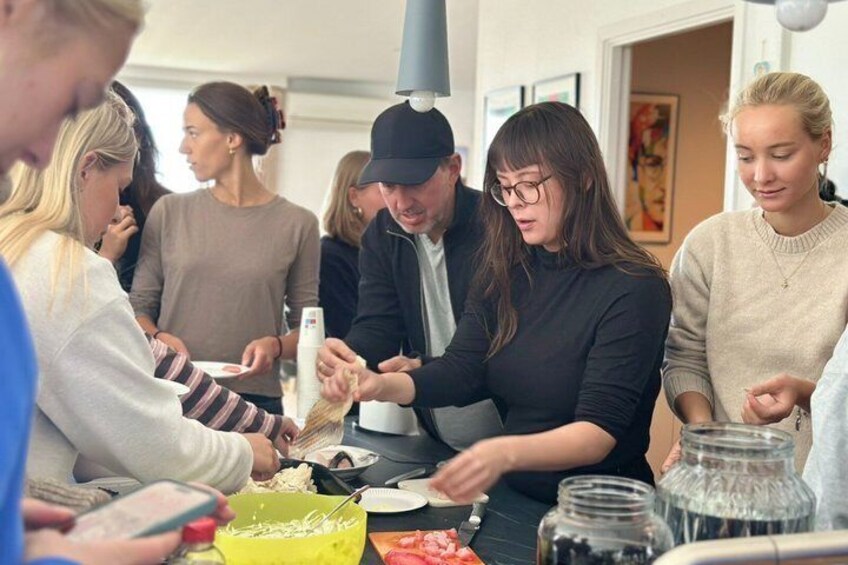 A group of people preparing food at a table with bowls, utensils, and jars. 4