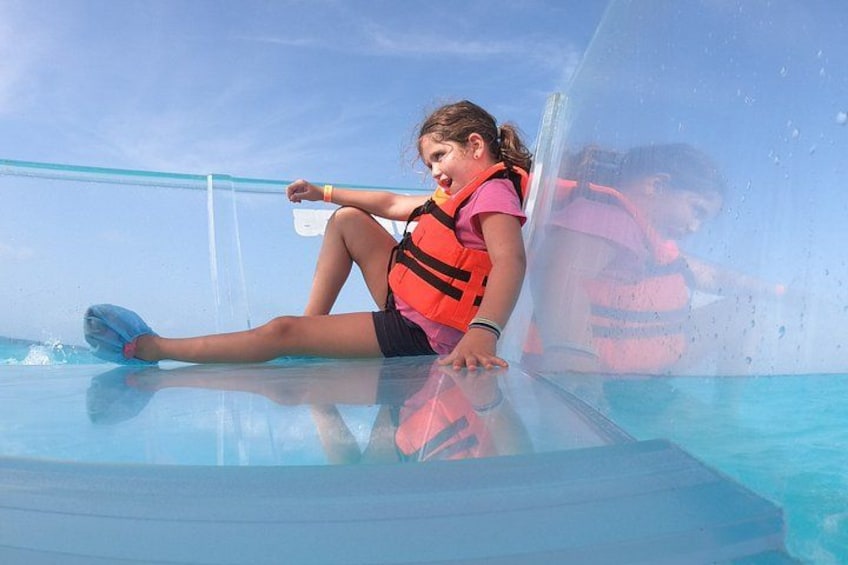 A person sitting on a transparent glass surface in a pool, wearing a life jacket. 3