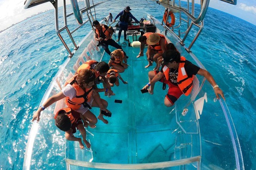 A group of people on a boat wearing life jackets, with clear blue water and a metal railing. 1
