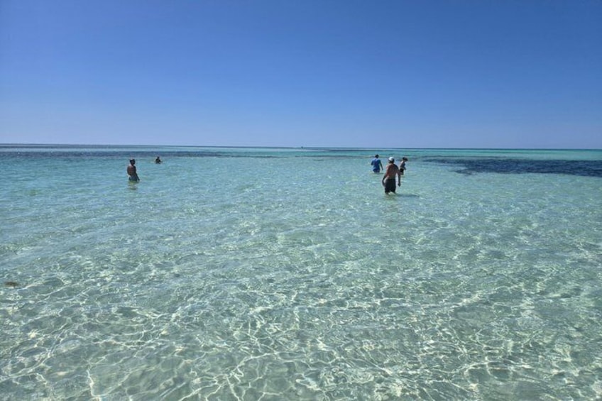A clear blue sea with people wading in shallow water. 2