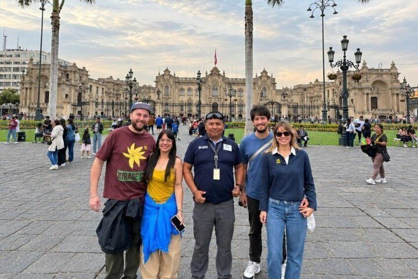 Un grupo de personas de pie en una plaza pública con edificios históricos al fondo. 1