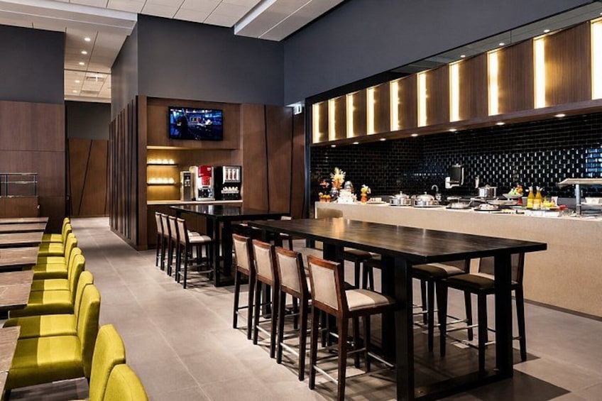Een modern restaurant met een lange eettafel, gele stoelen en een aan de muur bevestigde televisie. 5