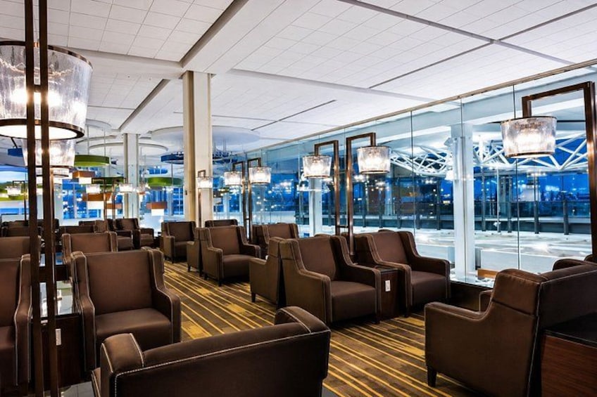 Een moderne lounge met lederen fauteuils, een kamerbreed tapijt met een patroon en grote ramen met uitzicht op een stadsgezicht. 4