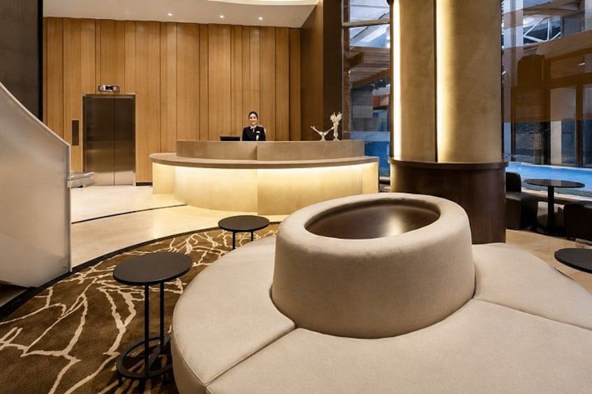 Een moderne lobby met een receptiebalie, een ruim ronde zithoek en een kamerbreed tapijt met dessin. 2