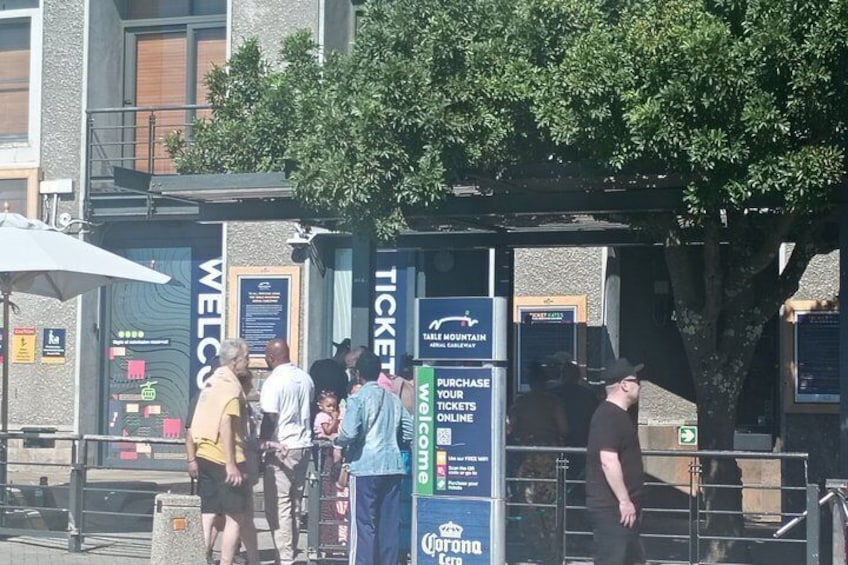 Ein Ticketschalter mit einem Schild, das 'Tickets online kaufen' anzeigt, und ein Baum im Hintergrund. 4