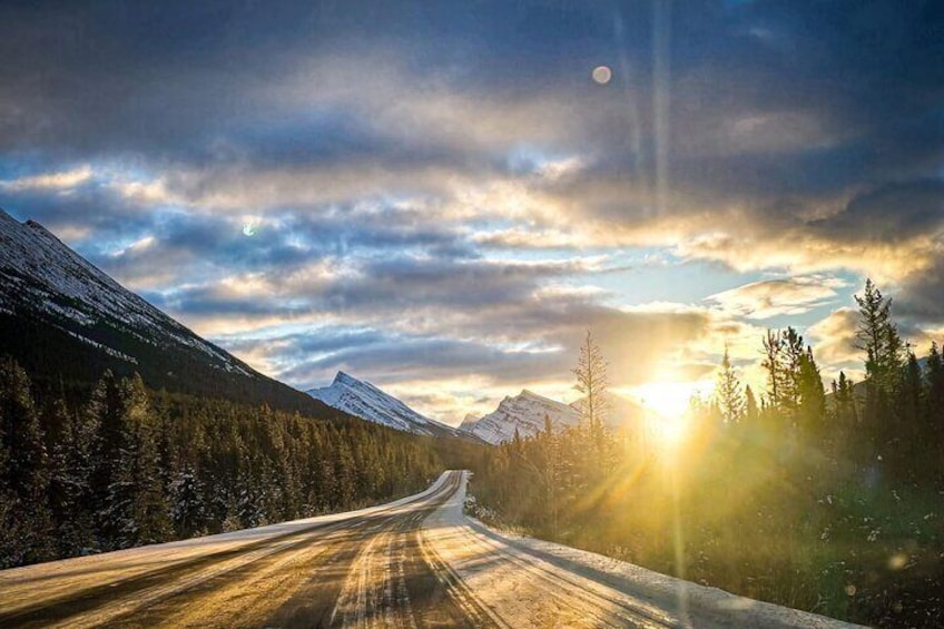 A snow-covered mountain road with a sunset in the background. 1