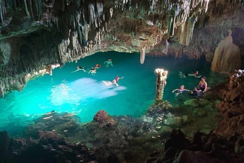 A group of people swimming in a natural cave pool surrounded by stalactites. 1