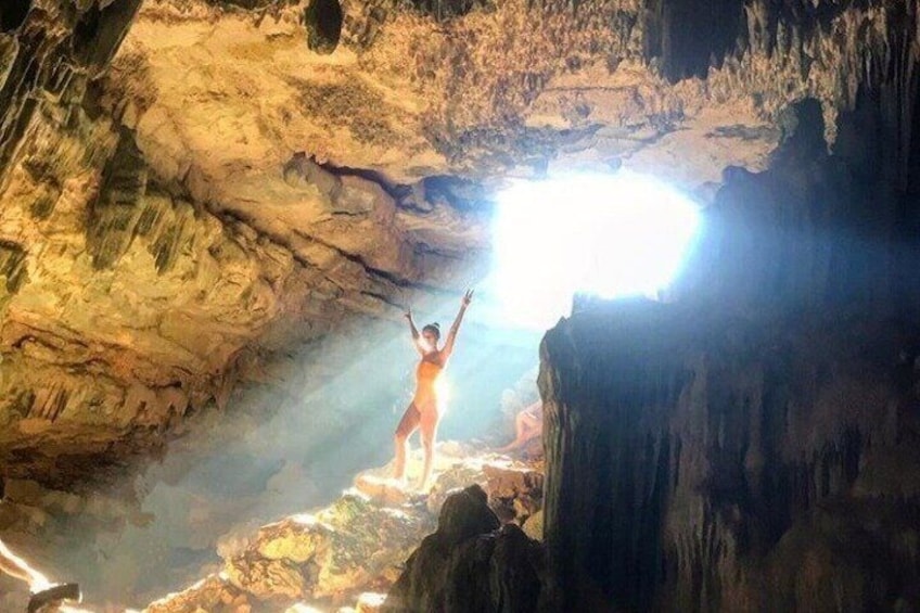 A person standing on a rock formation inside a cave with a bright light source above. 3