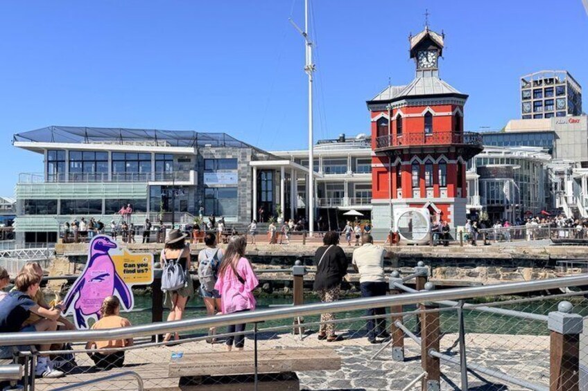 En strandpromenad med folk som promenerar, ett rött torn och moderna byggnader. 1
