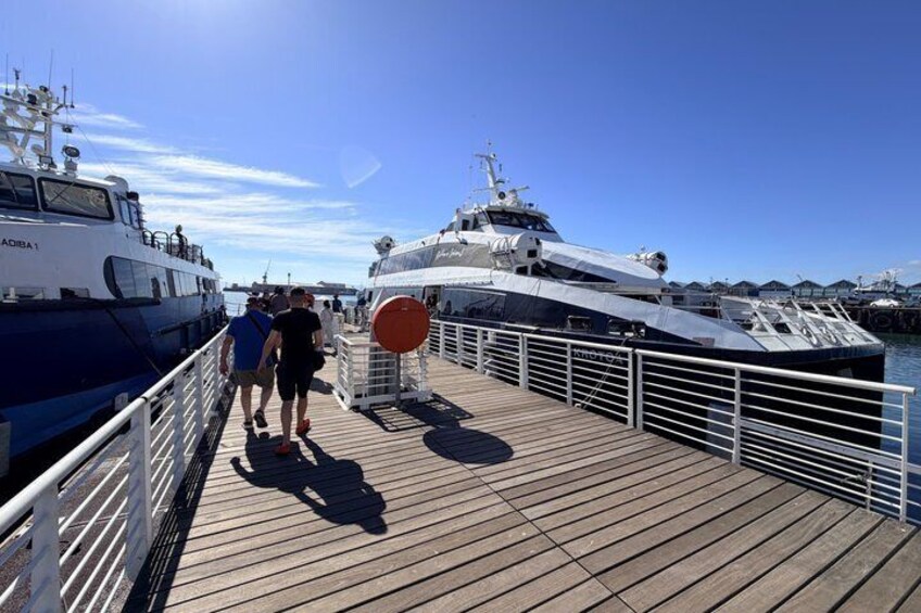 En träbrygga med folk som promenerar, en stor vit lyxyacht och en mindre båt som ligger förtöjd. 3
