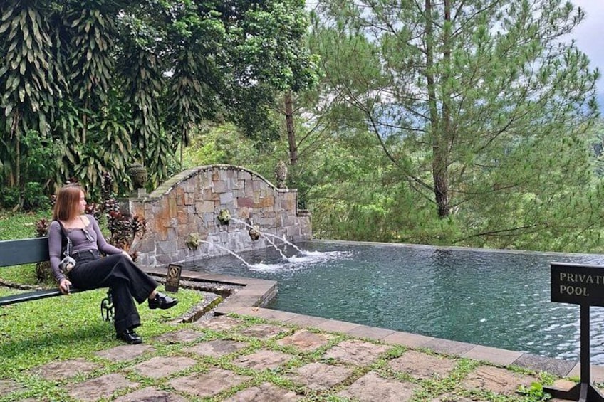 A person sitting on a bench by a private pool with a stone wall and greenery in the background. 5