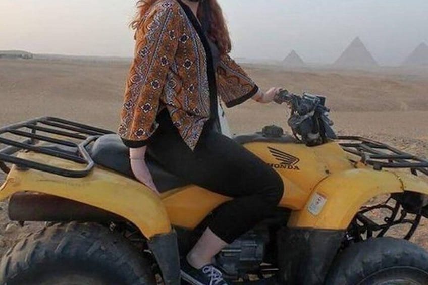 Une personne est assise sur un quad Honda jaune dans un désert, avec des pyramides en arrière-plan. 2