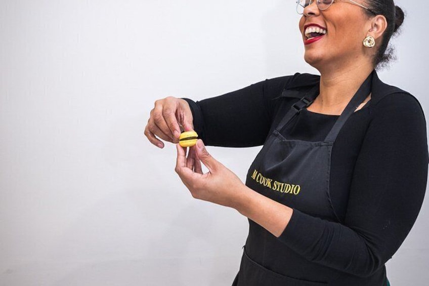 Une personne portant un tablier noir avec l’inscription « A Cook Studio », tenant un objet jaune. 1