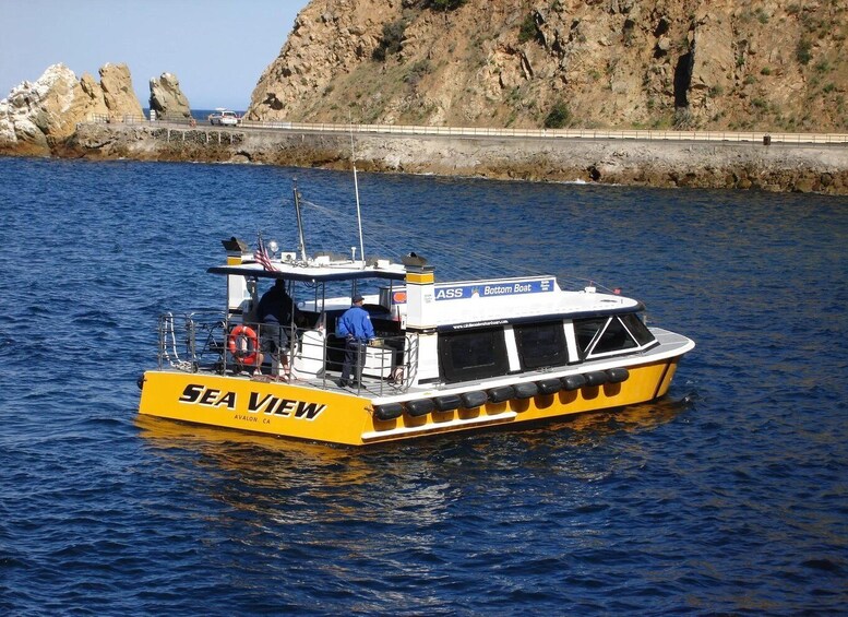 A yellow boat named SEA VIEW with 'Bottom Boat' written on the side, docked near rocky cliffs. 2