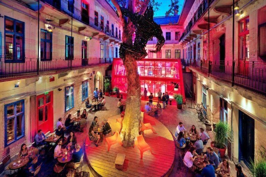 Un patio con un árbol grande, mobiliario exterior y edificios con balcones. 2