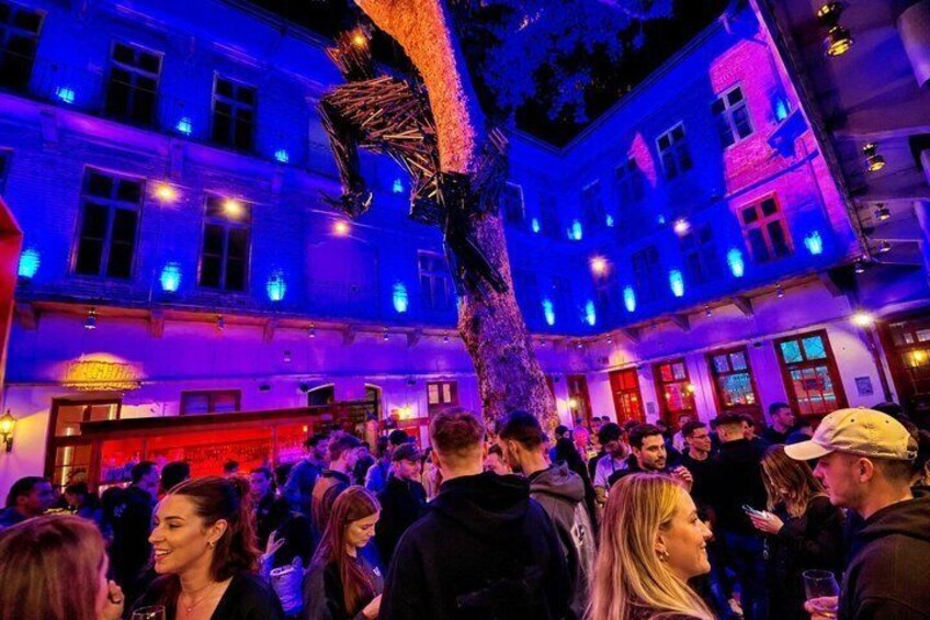 Un local interior abarrotado con gente socializando, iluminado con luces azules y moradas. 3