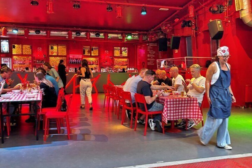 Een restaurant met rode stoelen en tafels, mensen aan het dineren, en een vrouw die loopt. 2