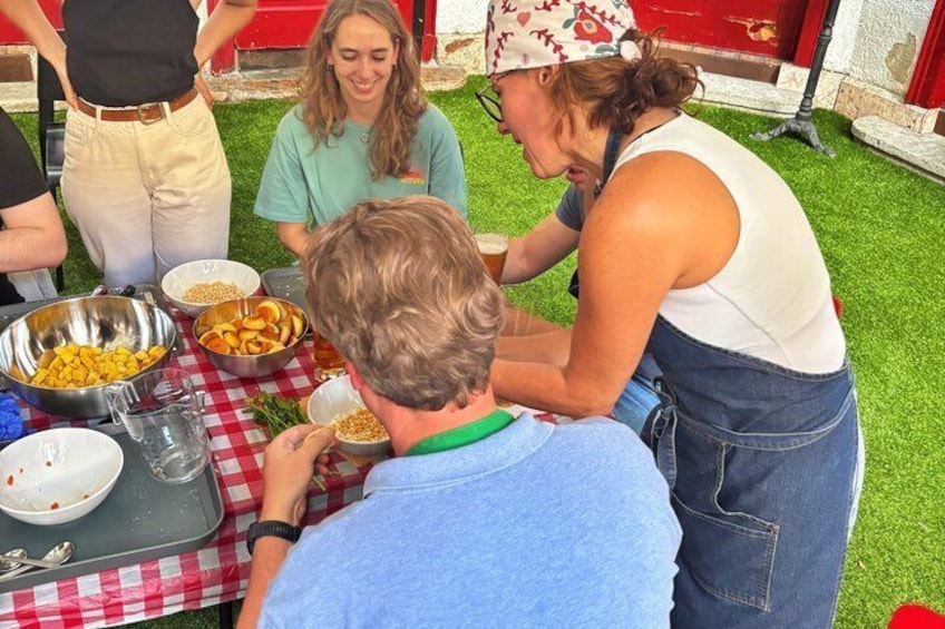 Een groep mensen is buiten, op een gazon, samengekomen rond een tafel met eten en drinken. 3
