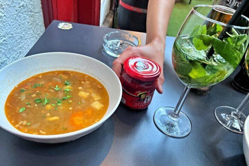 Un tazón de sopa, un vaso de bebida con menta y una lata roja sobre una mesa. 5