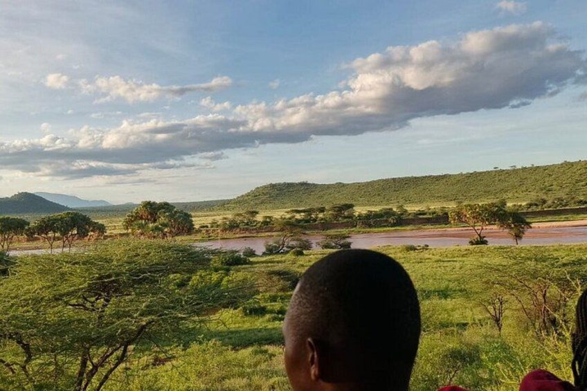 A savanna landscape with a river, trees, and distant hills. 2